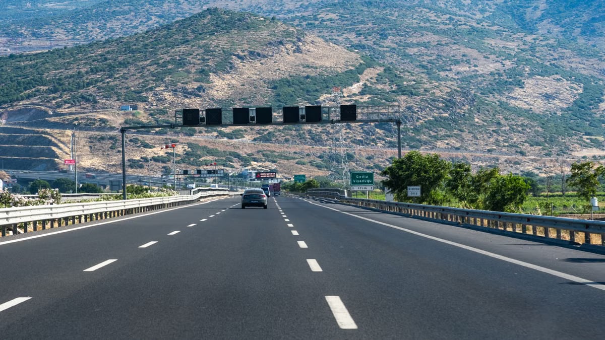 Long highway with cars traversing through rocky hills under blue skies, perfect travel scene.